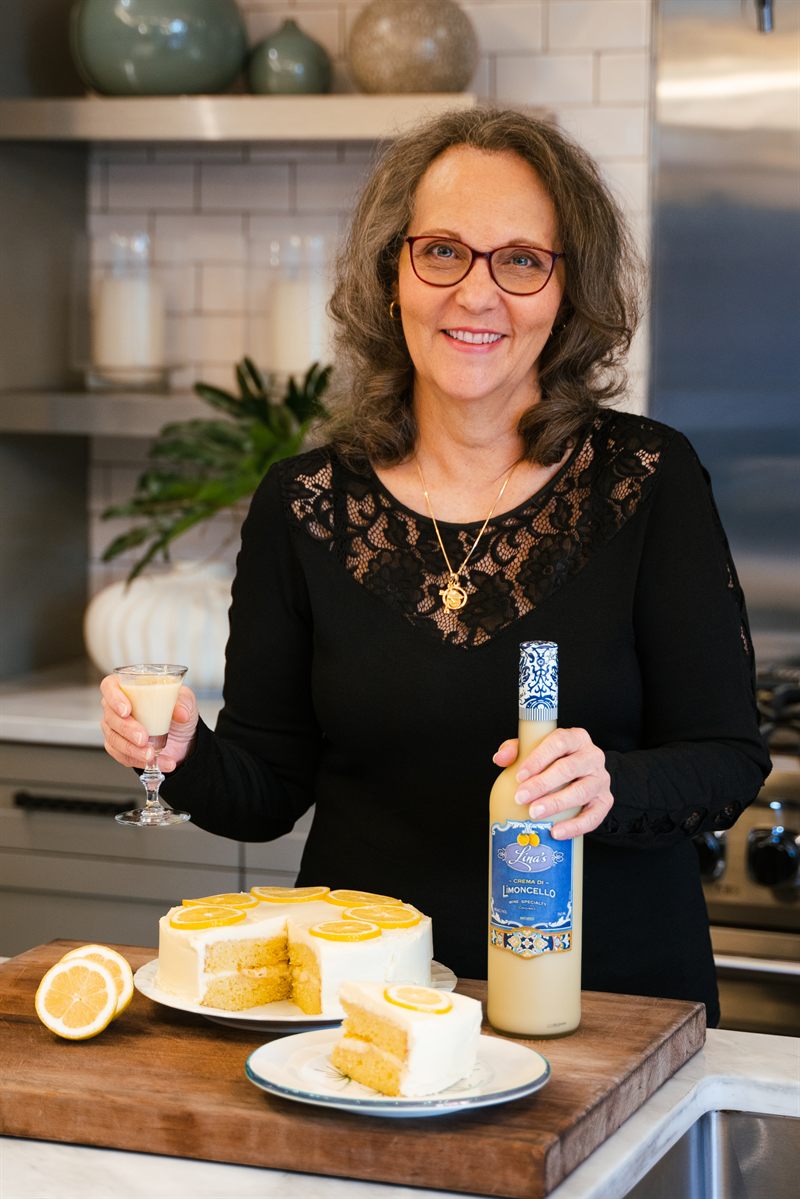 Lina holding a bottle of Lina's beside a lemon cake